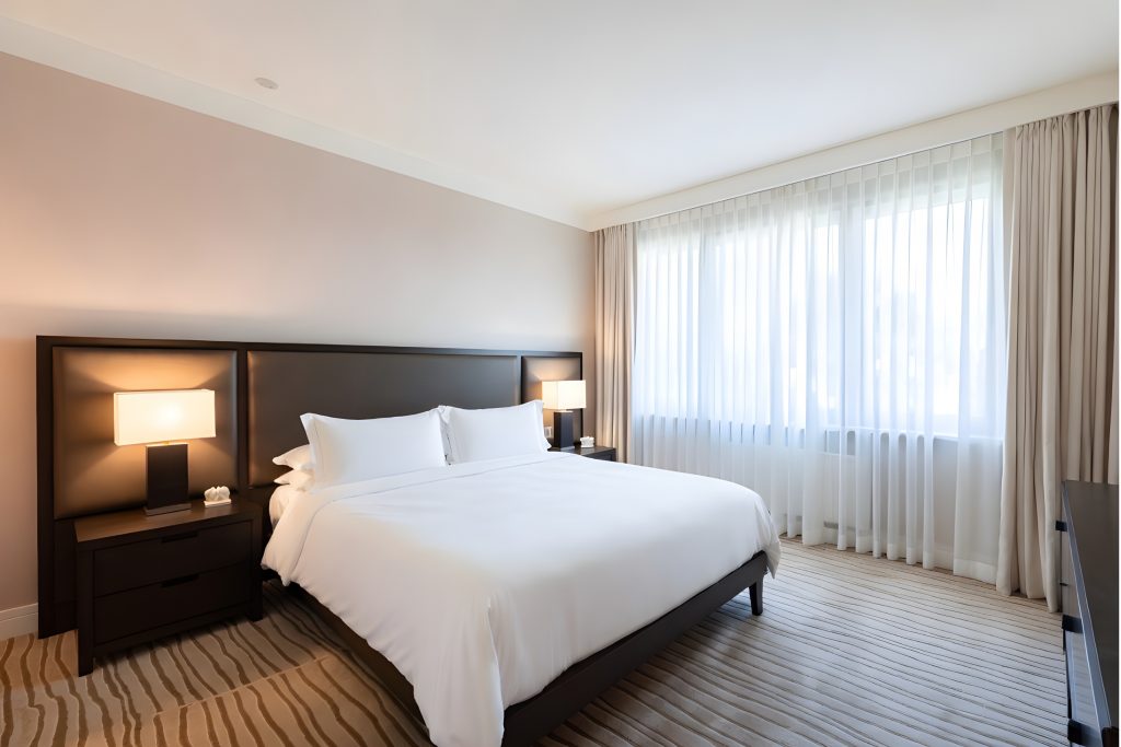 Modernes, helles Hotelzimmer mit großem Doppelbett, klaren Linien und reduzierter Einrichtung als Symbol für Professionalität und Struktur im Hotelbetrieb.