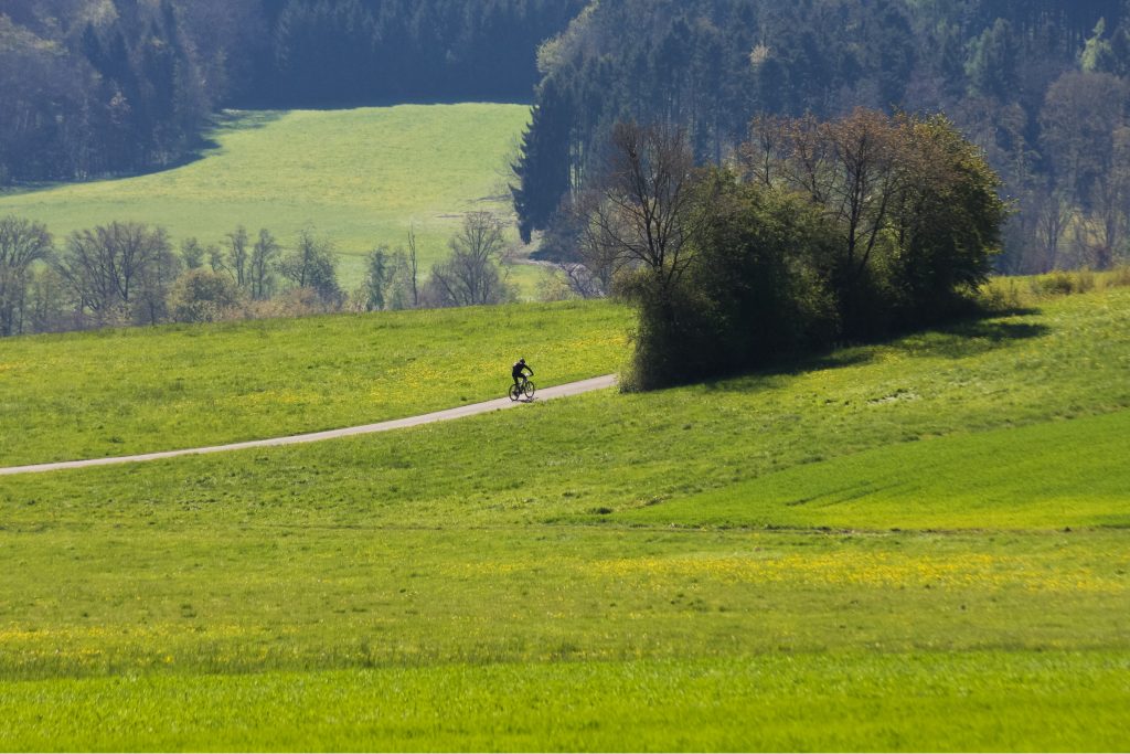Radfahrer auf einem Weg durch grüne Hügellandschaft im Mai am Obermain